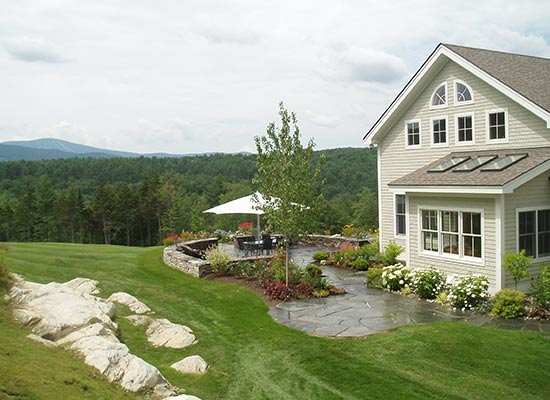 Picture of side of house with a patio and plantings surrounding the lawn