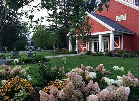 Picture of red barn style buildings with flowering bushes and large green lawn