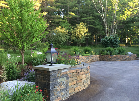 Picture of curved stone wall with trees and other plantings